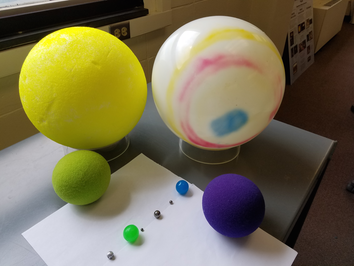 Ten colorful spheres made of different materials sit on a table.