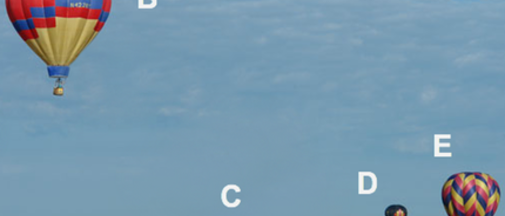 balloons_med.png Five hot air balloons at different distances in an open sky above a grassy field.